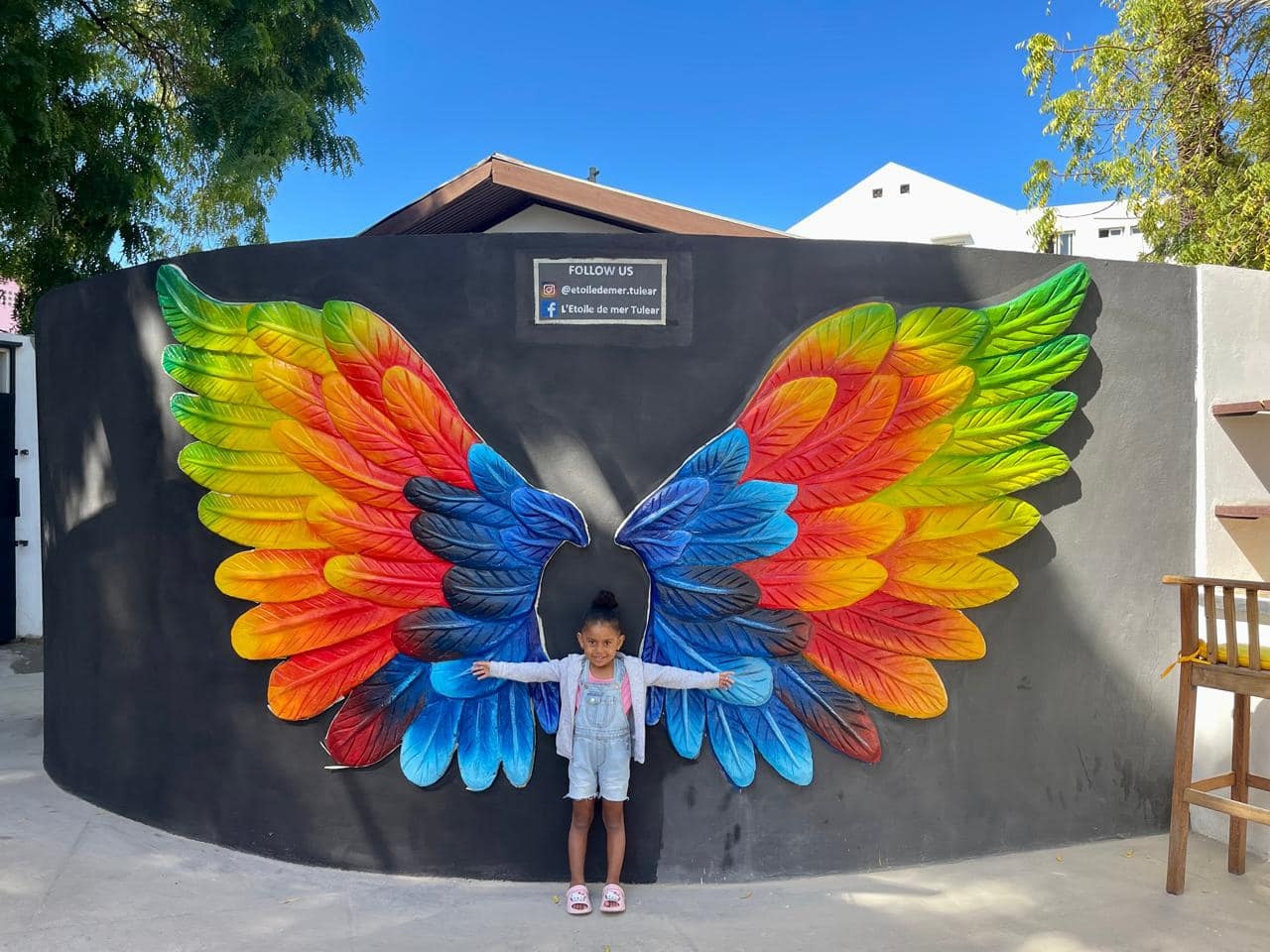 Enfant posant devant la fresque d'ailes colorées de L'Étoile de Mer Toliara